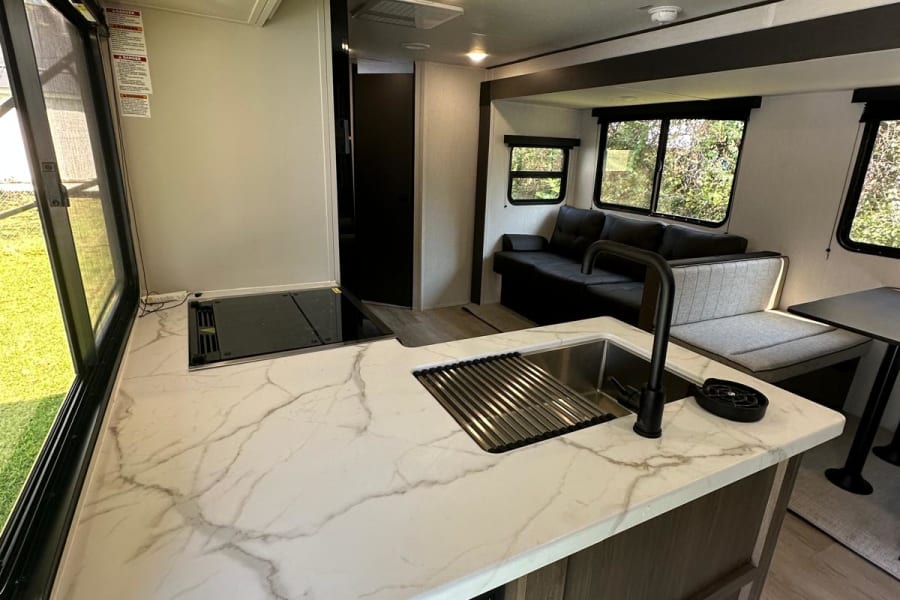 RV rental with bright, modern interior. Features a spacious kitchen island with marble-look counter, sleek cooktop, and comfy living area.