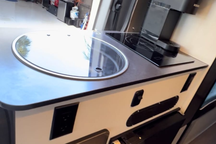 Experience comfort in this RV rental! Features a sleek compact kitchen with sink, induction cooktop, Keurig, and fridge.