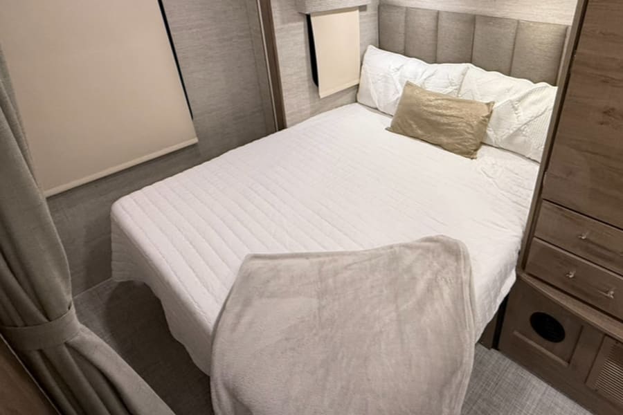 Cozy RV rental bedroom with a neat bed, soft blanket, and natural light. Perfect for travel comfort and relaxing interior.