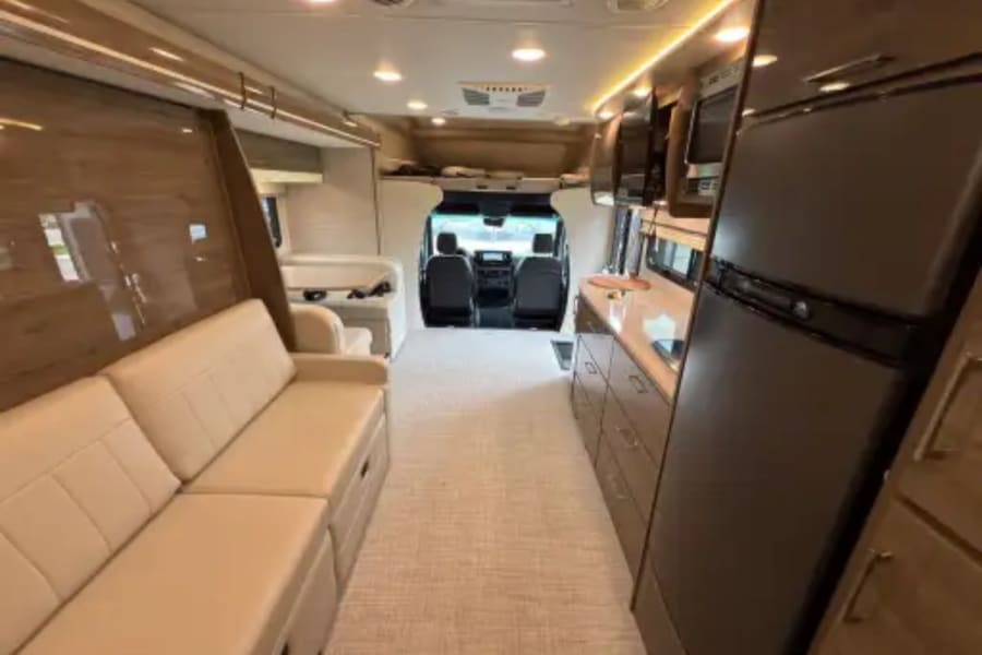 Spacious RV rental interior showcasing a cozy living area, full kitchen with fridge, and front cab view.
