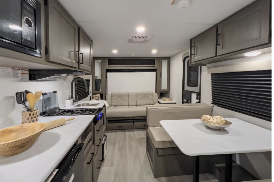 Inside this inviting RV rental, a compact kitchen with a stove and microwave, a dinette, and a sofa offer modern comfort.