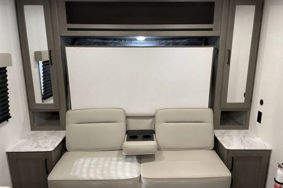 Modern rv rental interior: sofa with cup holders, beneath a wall-mounted Murphy bed, flanked by storage cabinets.