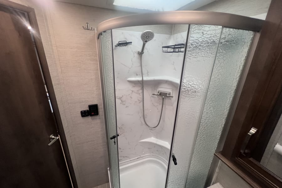 RV rental's compact, clean shower featuring a handheld showerhead, marbled walls, and textured glass doors for comfort.