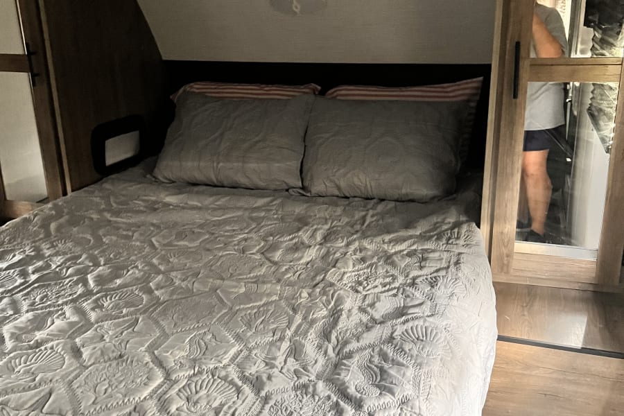 RV rental bedroom with a cozy bed featuring a quilted sea-themed comforter and mirrored closet visible.