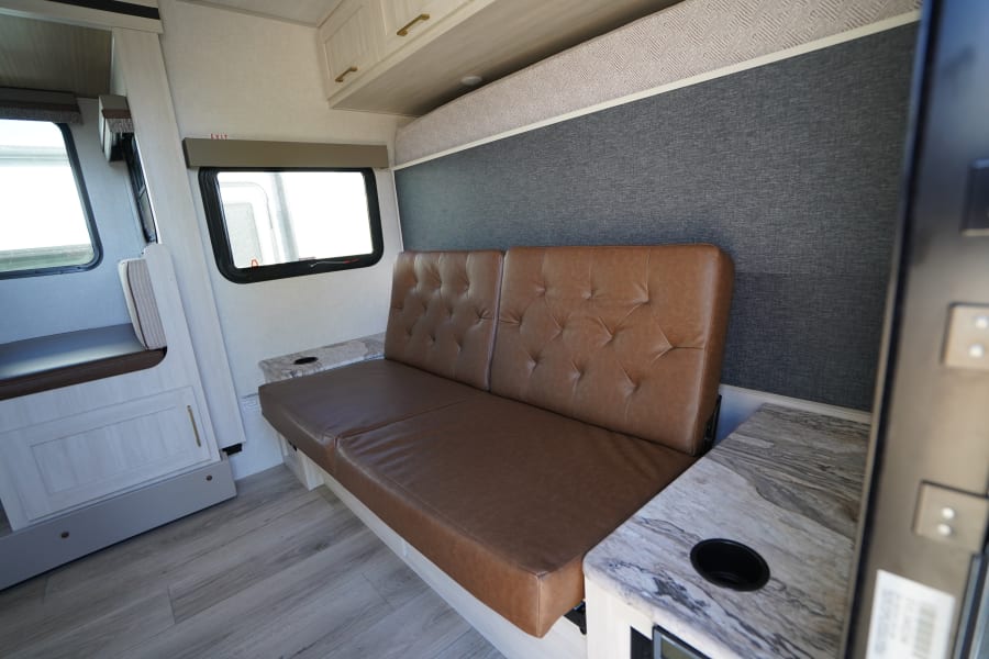Step inside this RV rental's inviting living space, featuring a brown tufted sofa, dinette, and light wood cabinetry.