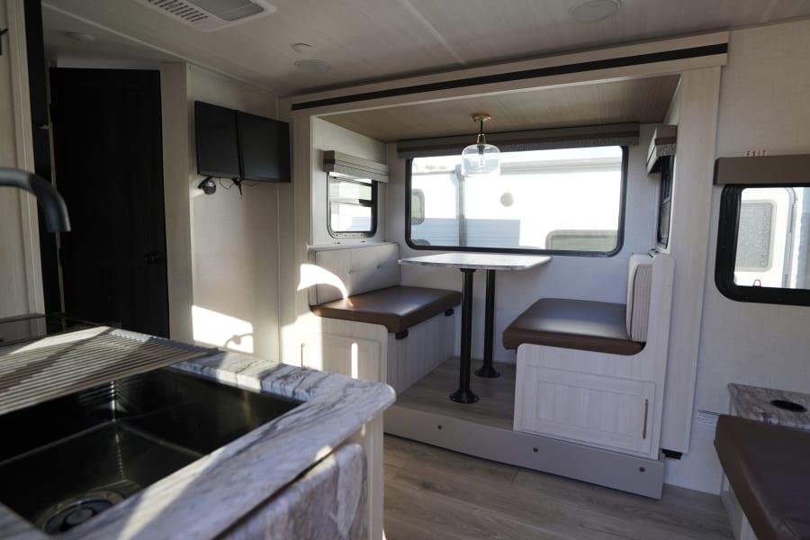 Spacious and modern RV rental interior featuring a kitchen sink, dinette booth with table, and large windows. Perfect for travel!