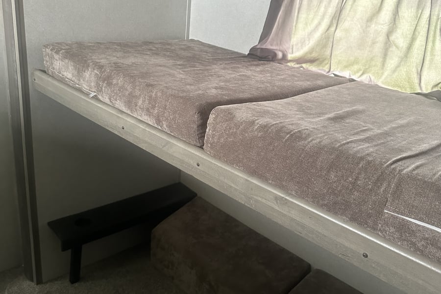 Inside an RV rental: a cozy bunk bed with soft cushions, window with curtains, and lower seating options.