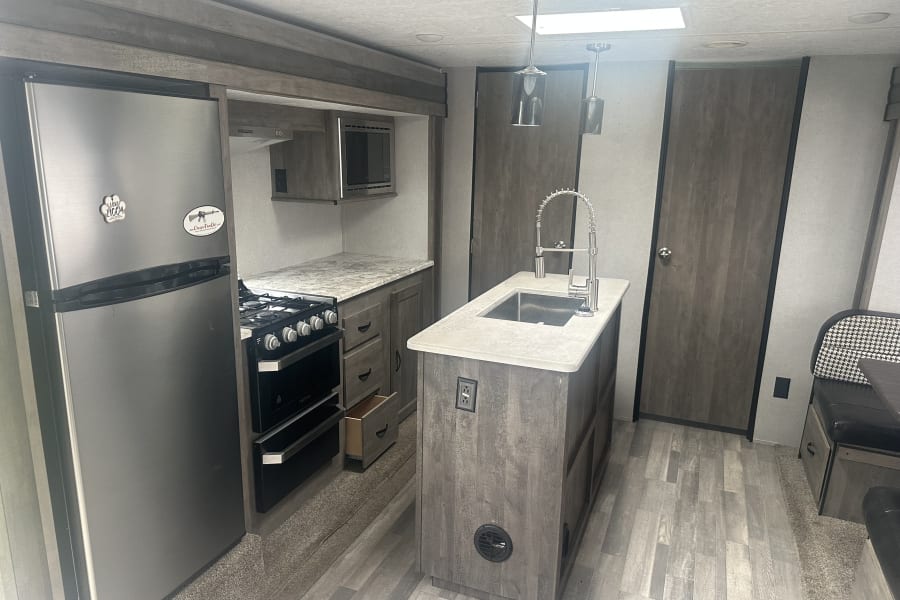RV rental kitchen with stainless appliances, wood-look cabinets, island sink, and dining area.