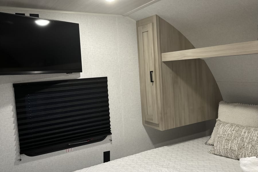 Modern RV rental bedroom with a cozy bed, wall-mounted TV, skylight, and storage. Perfect for comfortable journeys.