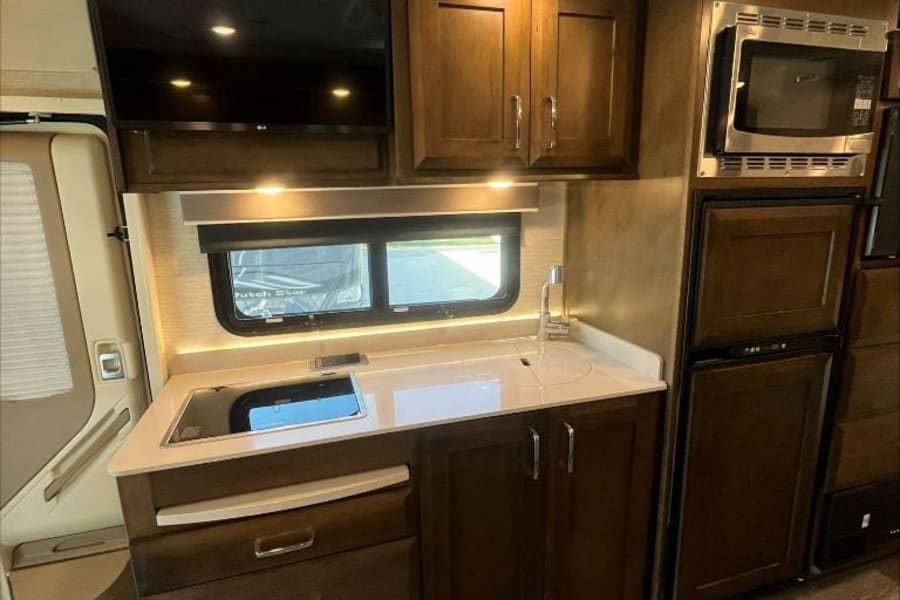 Modern rv rental kitchen featuring built-in microwave, refrigerator, induction cooktop, and ample cabinetry.