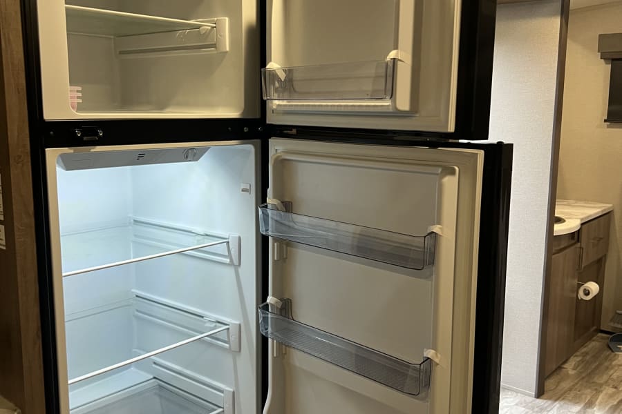 Bright, open RV rental refrigerator with separate freezer, clean shelves, and door storage, ideal for road trips.