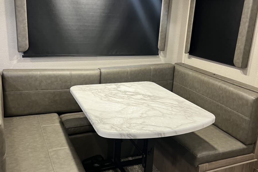 Cozy RV rental dinette featuring gray booth seating, a faux marble table, and blackout window shades.