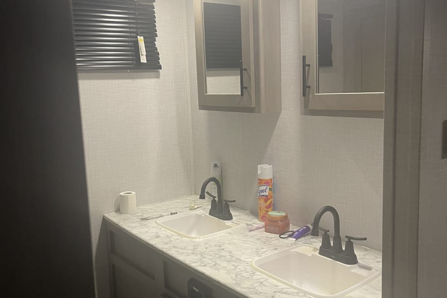 An RV rental bathroom showing a double vanity with two sinks, medicine cabinets, and bright overhead lighting.