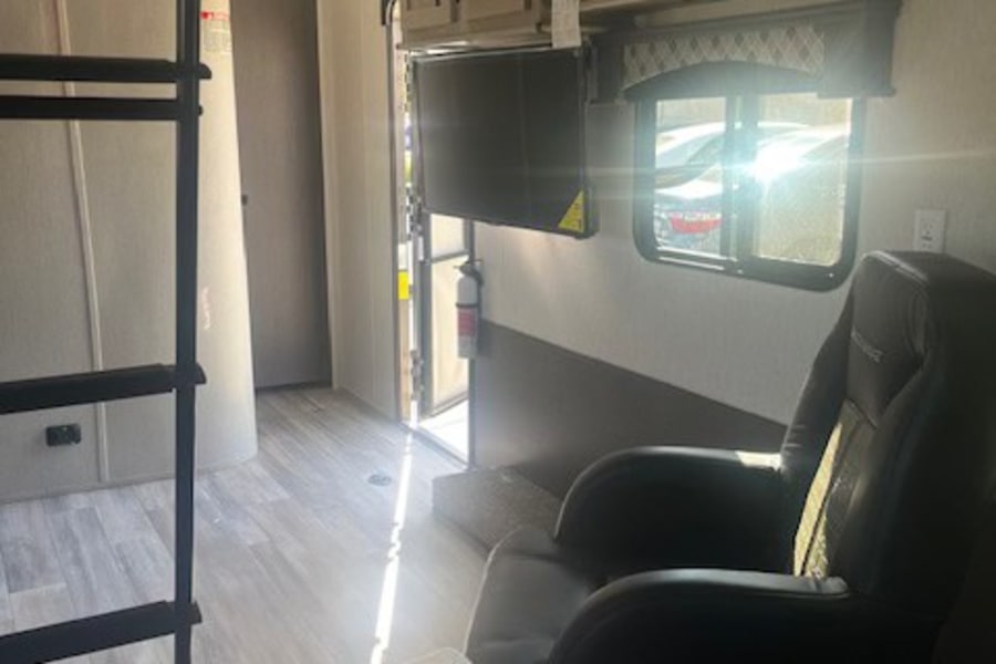 Spacious RV rental interior: bright living area with a comfortable recliner, TV, overhead cabinets, and bunk ladder.