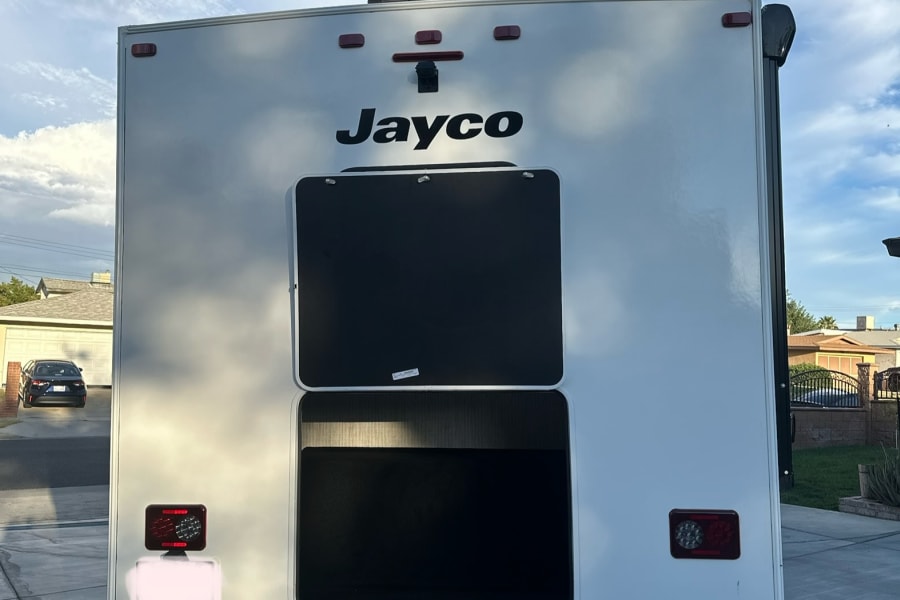 Rear view of a white Jayco RV rental under a blue sky, featuring black bunk windows and a tow hitch, ready for adventure.
