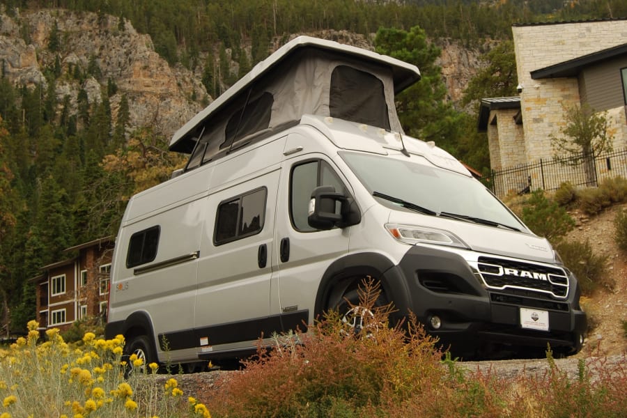 Silver Solis pop-top RV rental parked in a stunning mountain setting with pine trees, perfect for your next adventure.