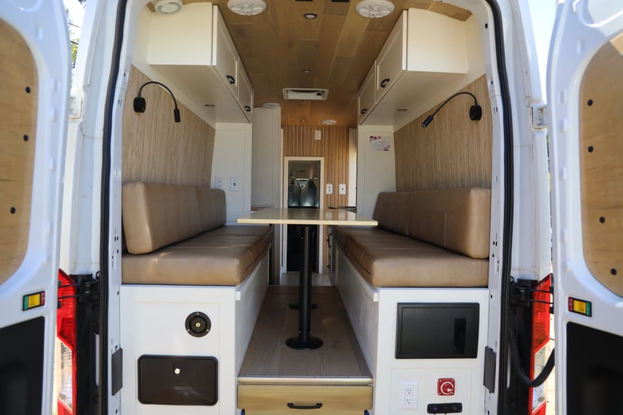 Experience comfort in this modern RV rental's dinette area, featuring wood accents, overhead storage, and ample seating.