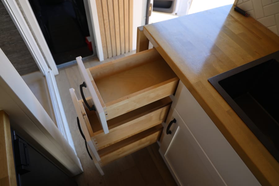 RV rental kitchen with open drawers, a sleek black sink, and a light wooden countertop inside a camper van.