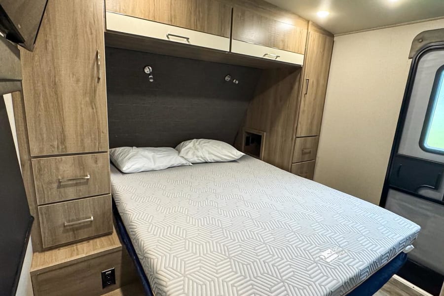 RV rental interior: A cozy bedroom with a patterned mattress, ample storage cabinets, and an AC unit for comfort.