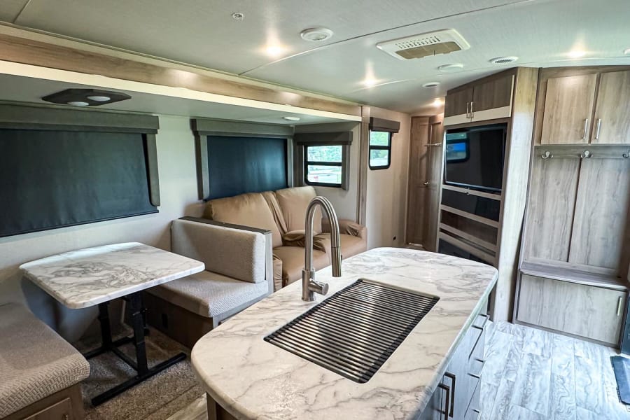 Bright RV rental interior with a marble-look kitchen island, dinette, and cozy sofa. Features modern cabinetry and wood-style flooring.