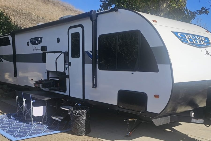 White Cruise Lite Platinum RV rental set up for outdoor living with a blue mat & chairs. Perfect for your next travel adventure.