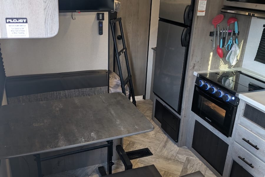 This RV rental's interior boasts a dinette, kitchen with stove, fridge, TV, and a ladder leading to upper bunks.