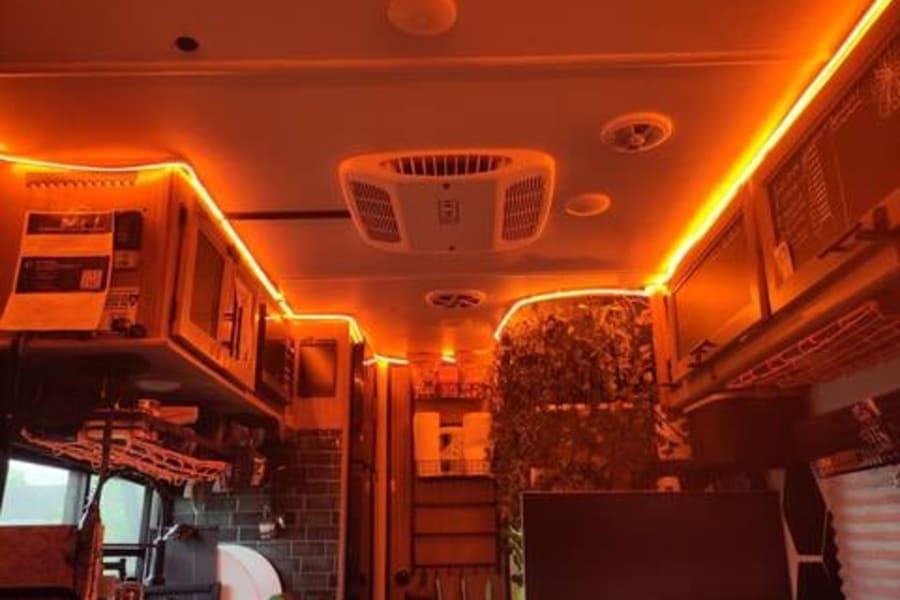 Warm orange LED lighting creates a cozy ambiance in this RV rental's modern interior, featuring a kitchen and lounge area.
