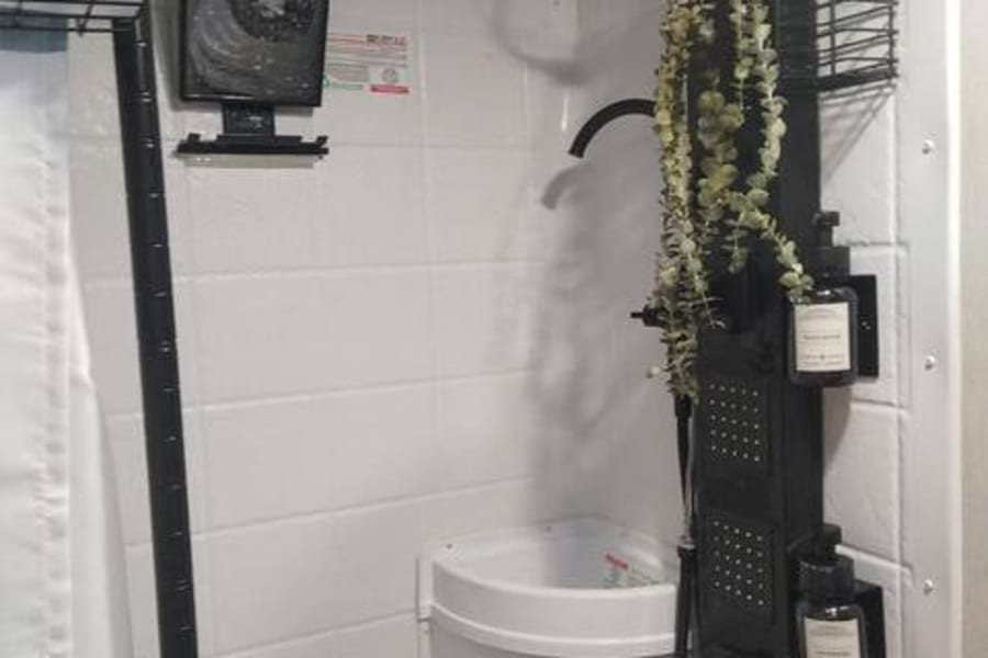 Modern RV rental shower featuring black rainfall head, integrated panel, compact corner sink, and decorative plant.
