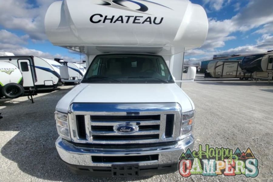 A white Thor Chateau Class C motorhome, ready for rv rental adventures. Parked in a lot with other RVs under a blue sky.