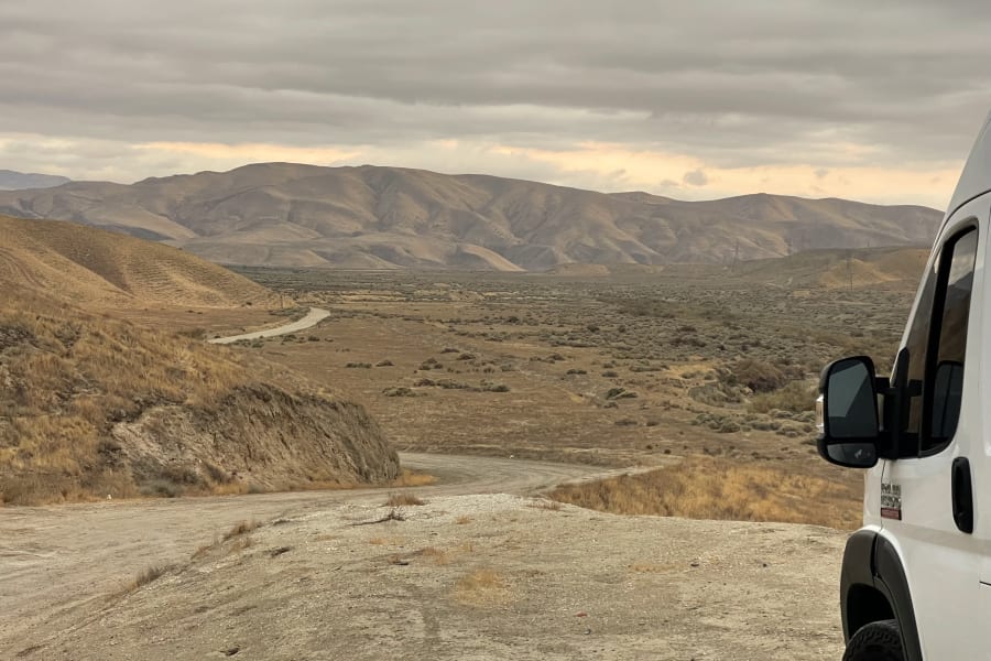 RV rental exploring a vast desert landscape with mountains and a winding dirt road under cloudy skies. Great for adventure travel.