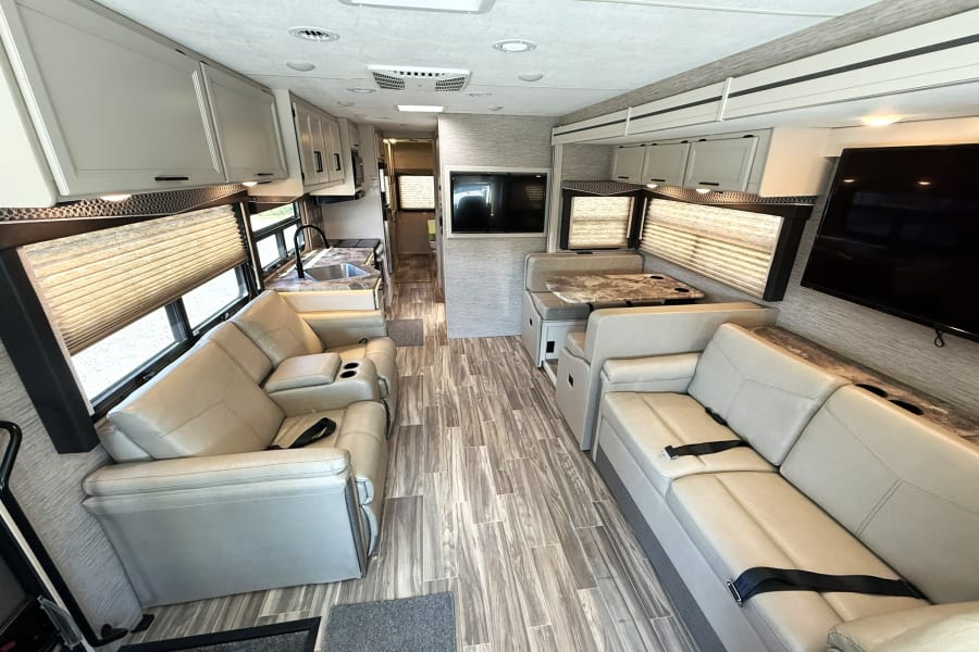 Spacious, modern rv rental interior with living area, kitchen, dinette, and wood-look floors. Ideal for your next journey.
