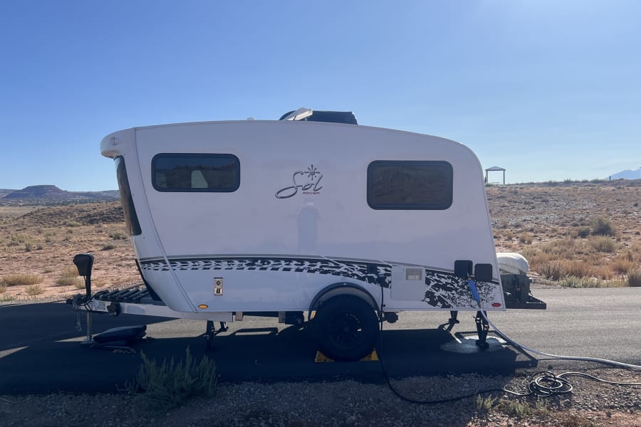 White Sol Rover rv rental trailer with hookups, parked in a sunny desert campsite. Ideal for your next outdoor adventure.