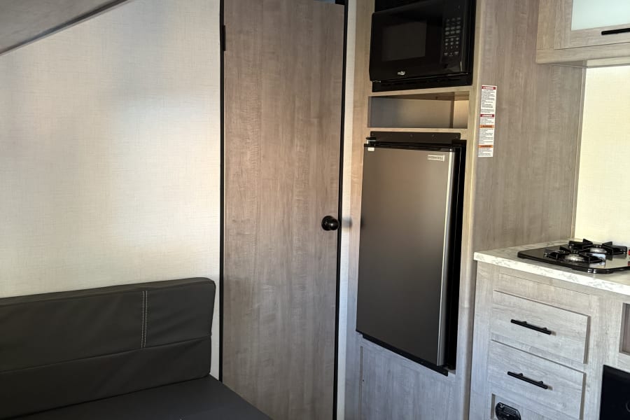 RV rental: interior view of a bright kitchen and dinette, featuring microwave, fridge, stovetop, and bench seating.