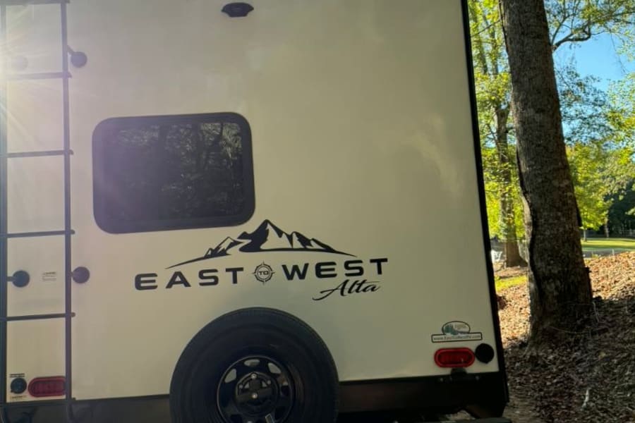 Rear view of an East to West Alta travel trailer, ideal for your next rv rental. Parked in a sunny, wooded campsite.