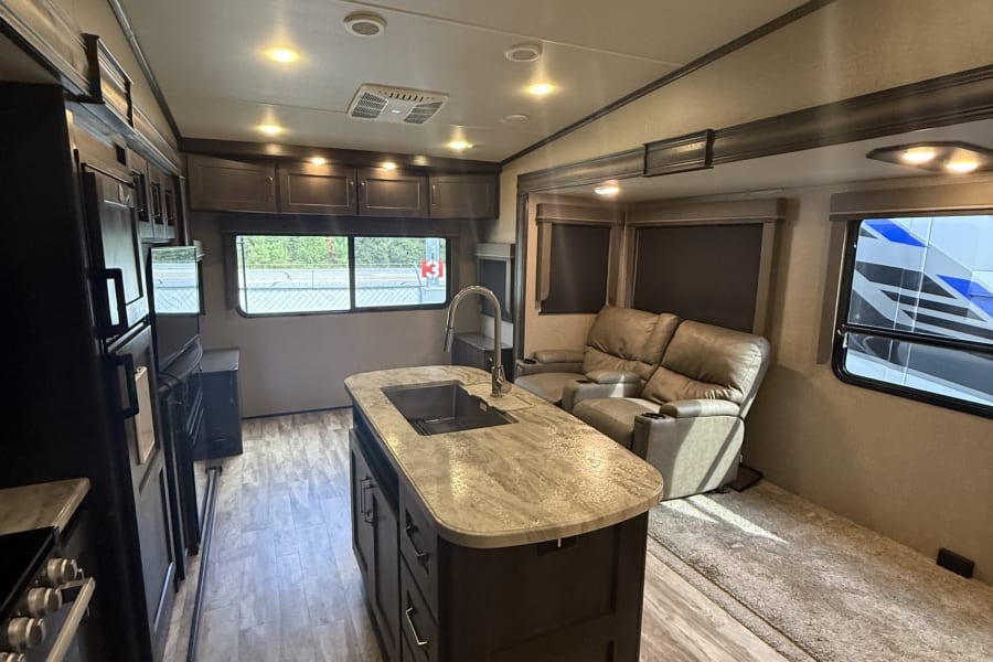Clean RV rental interior featuring a kitchen island with sink and comfortable living area with recliners, perfect for travel.