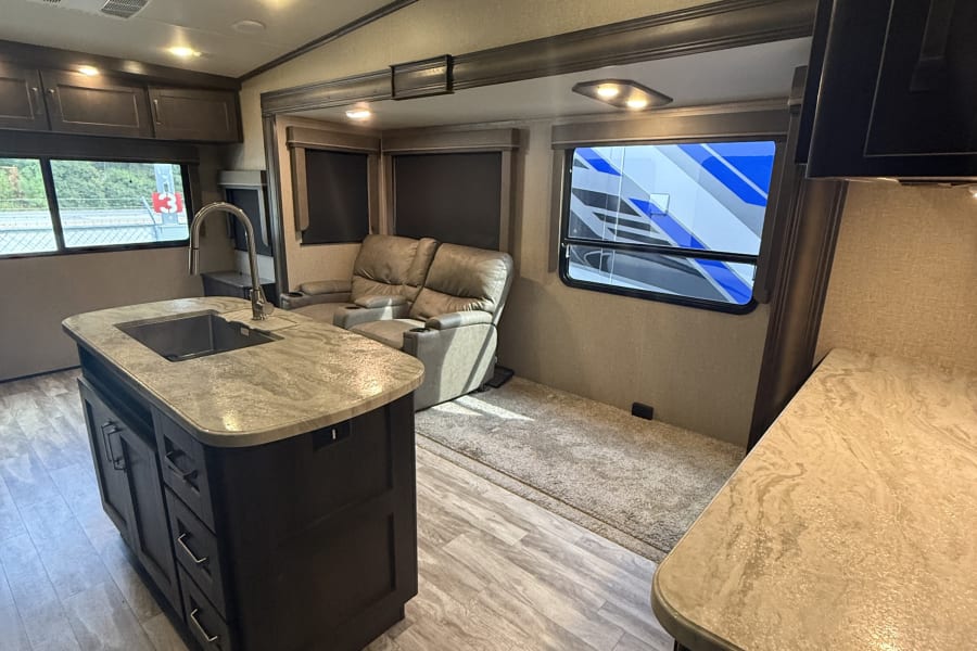 Modern RV rental interior featuring a functional kitchen island, comfortable living area, and bright lighting.