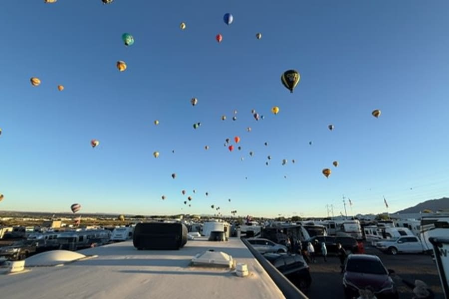 Dozens of colorful hot air balloons soar above a massive RV park. Imagine this breathtaking festival view from your rv rental!