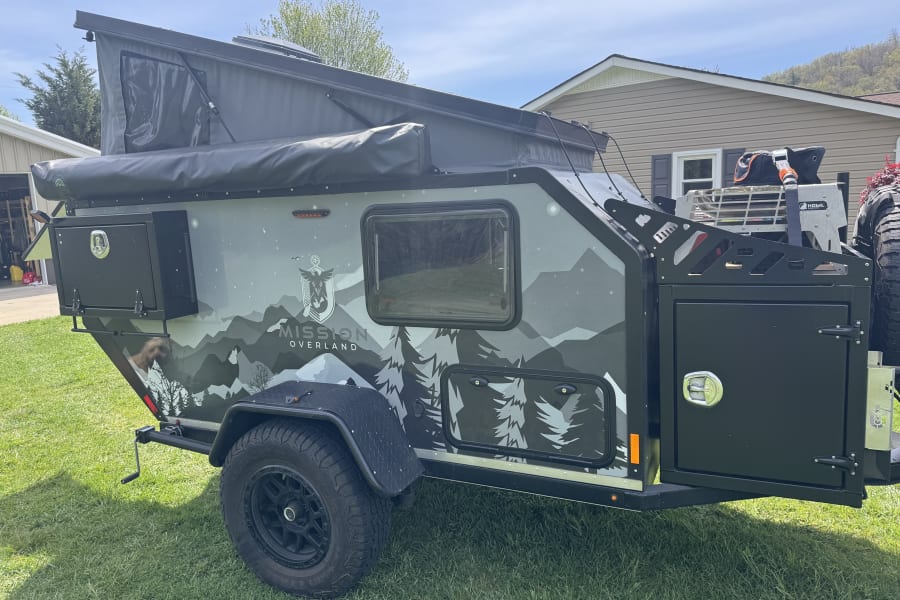This rugged Mission Overland trailer, featuring mountain graphics, pop-up tent, and off-road tires, is ideal for your next RV rental adventure or off-road camping trip.