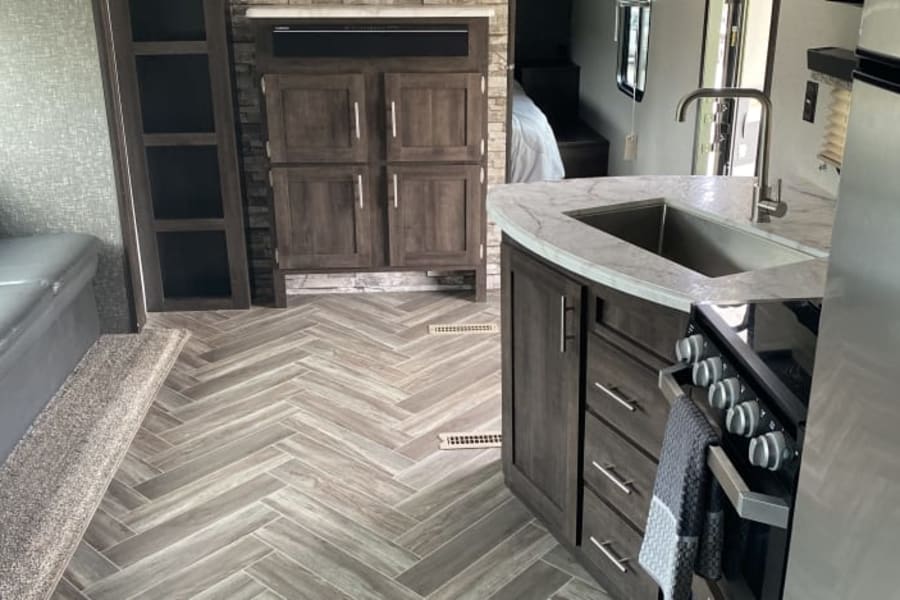 Inside an RV rental: a modern kitchen with a sink, stove, wood-look cabinets, and chic herringbone flooring throughout.