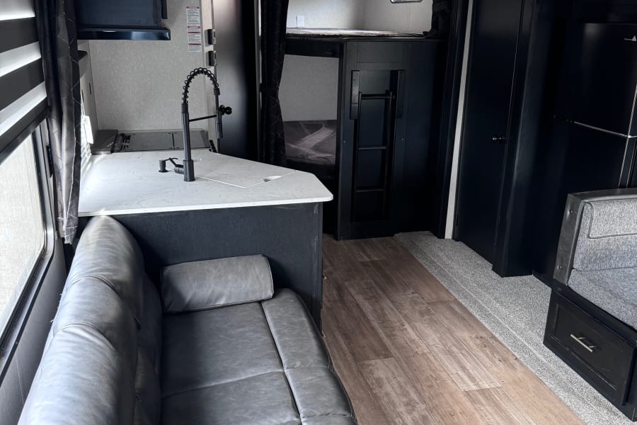 Inside a modern **rv rental** with a sleek kitchen, comfy faux leather sofa, and bunk beds. Features wood flooring & carpet.