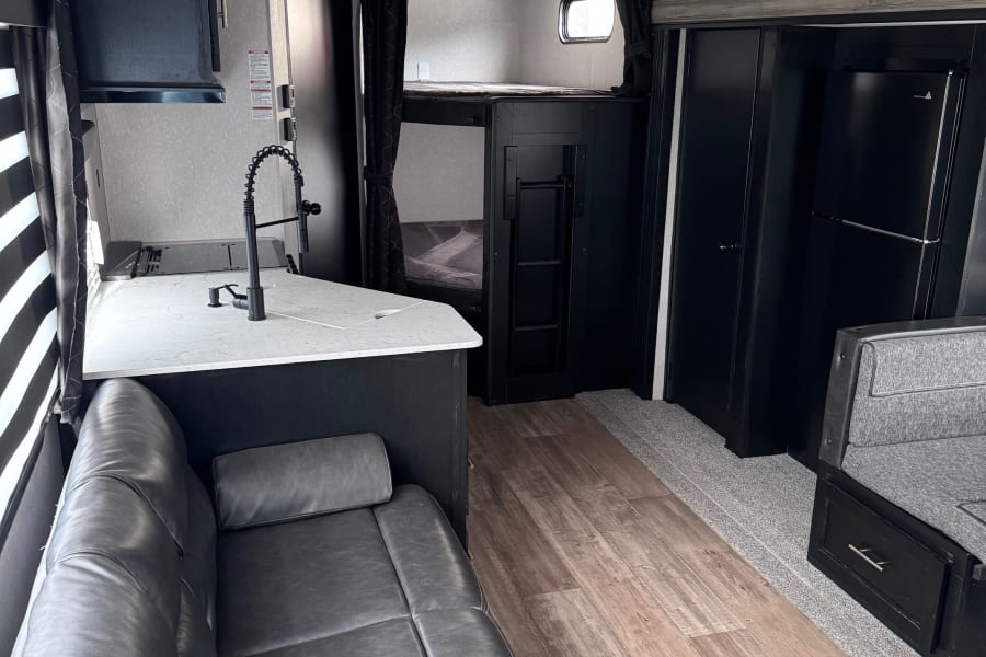 RV rental interior featuring a kitchen with sink, cozy gray sofa, bunk beds, and a mix of wood-look flooring and carpet.
