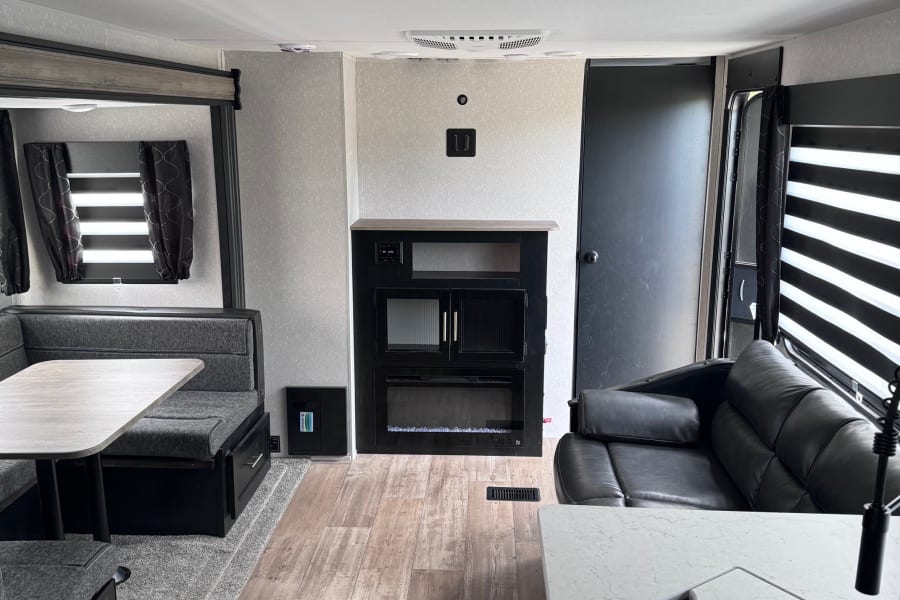 Modern rv rental interior: compact living, dining, and kitchen area with dark furniture and wood-look floor.