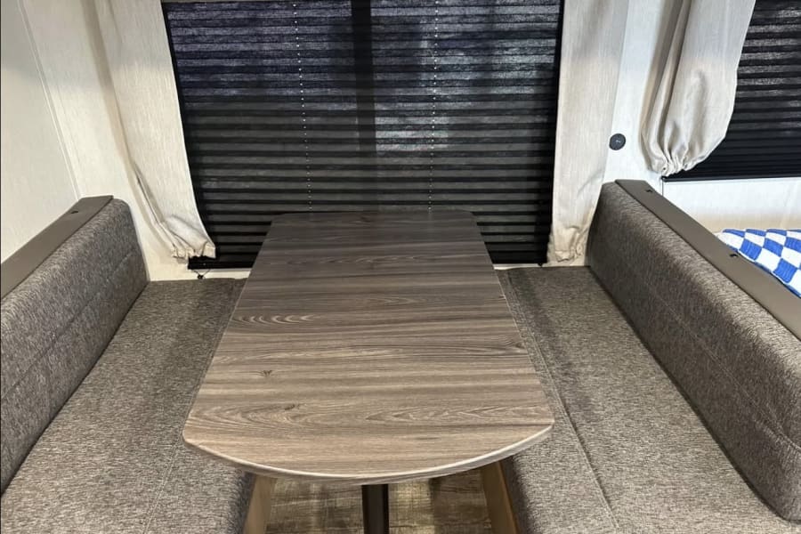 Cozy RV rental dinette featuring gray fabric benches and a dark wood-grain table, ideal for meals or relaxing.