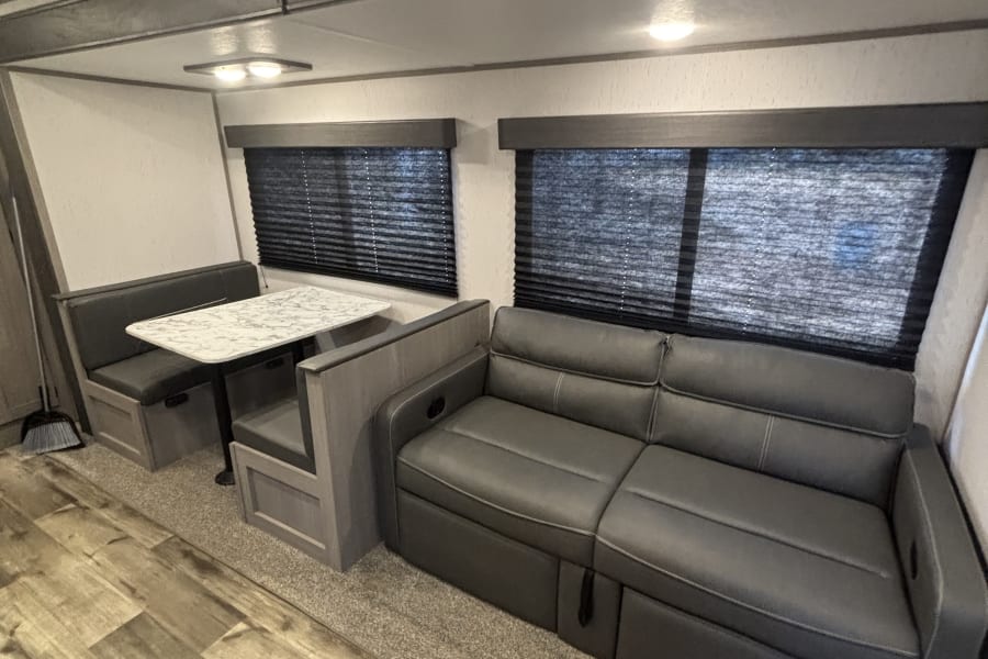 Step inside this RV rental, showcasing a gray dining booth, plush sofa, and blended wood-look and carpet flooring.