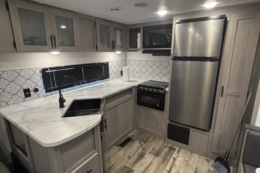 Modern RV rental kitchen with sleek grey cabinets, marble-look countertops, stainless appliances, and patterned backsplash.