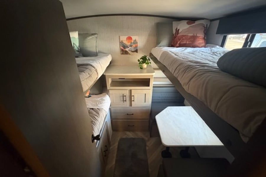 RV rental's cozy bunk bed area: two sets of beds, a central storage cabinet, and a pull-out table for travelers.