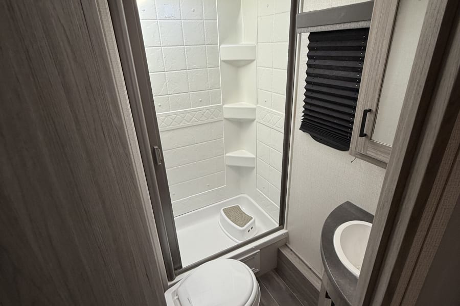 RV rental bathroom featuring a stand-up shower, toilet, sink vanity, and skylight above, with modern wood-look flooring.