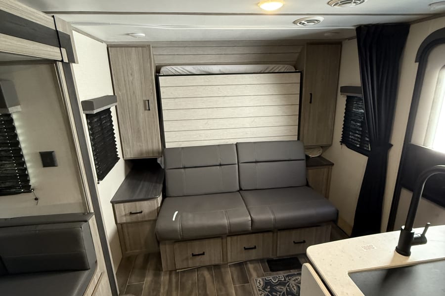 Modern RV rental: a flexible living area featuring a pull-down bed, comfy sofa, dinette, and compact kitchen.