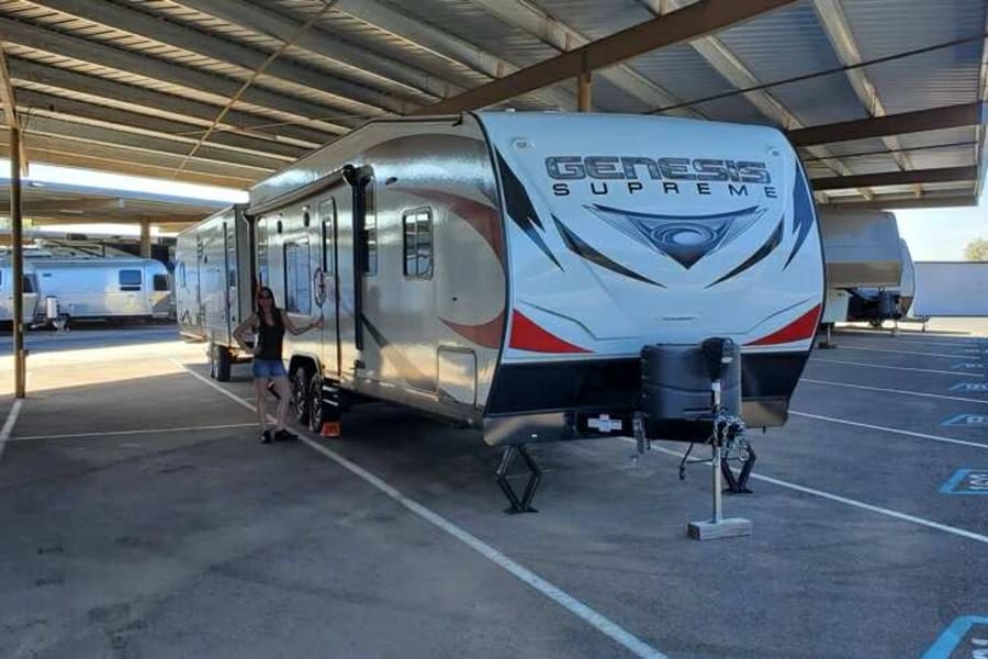Enjoying the outdoors with an RV rental! A woman stands by a large Genesis Supreme travel trailer in covered parking.