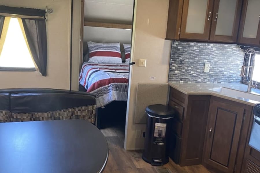 RV rental interior: A modern kitchen with tile backsplash, cozy bedroom with striped bedding, and dining space. Hardwood floors throughout.